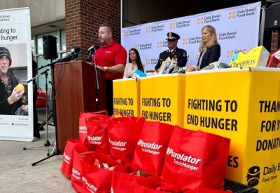 Personb speaking at a podium next to food donation boxes